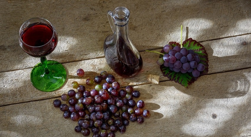 Tavola con un bicchiere e una bottiglia di vino rosso e uva